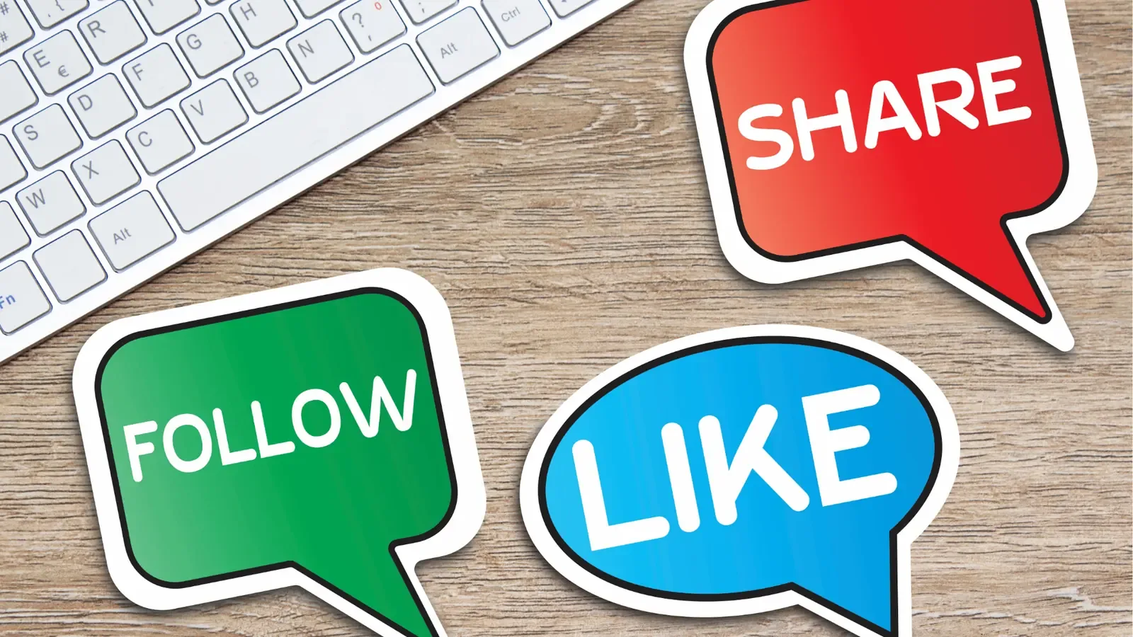FOLLOW, LIKE and SHARE speech-bubble stickers laid out on a desk beside a keyboard